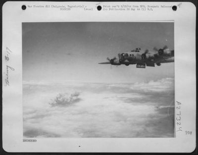 Completing a run over the aircraft plant and Airdrome at Belgrade, Yugoslavia is a Boeing B-17 Flying Fortress of the 15th AAF. The smoke from the target can be seen rising through the clouds at the left.